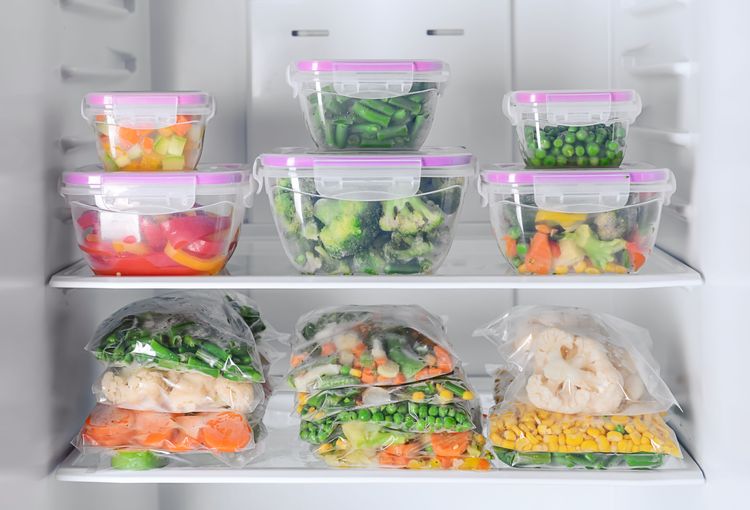 mehrere Kunststoffboxen mit buntem gefrorenem Gemüse in offenem Tiefkühlschrank