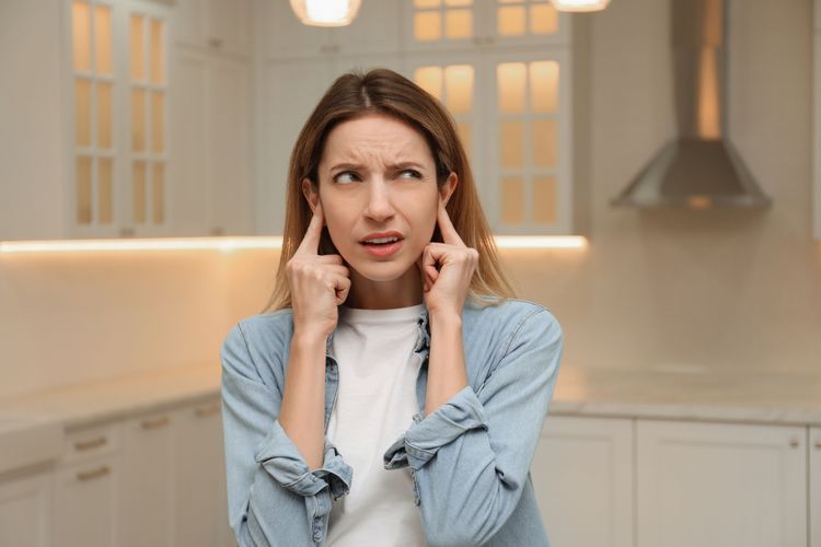 Frau in Küche bedeckt ihre Ohren mit Fingern weil es zu laut ist