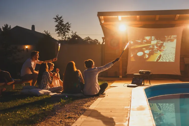 Freundesgruppe blickt auf eine bespielte Leinwand im Garten.