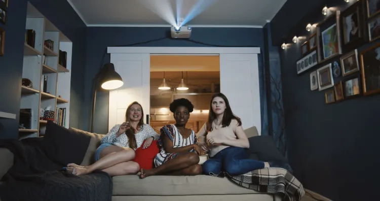 3 Freundinnen verfolgen eine Filmprojektion im Wohnzimmer.