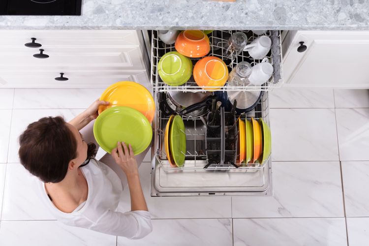 Junge Frau räumt buntes Geschirr aus Spülmaschine