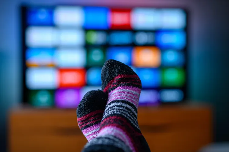 Im Vordergrund, die bunten Socken einer Person, die sich Appübersicht eines Fernsehers anschaut, der im Hintegrund verschwommen zu sehen ist.