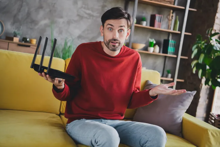 Junger Mann mit fragendem Gesichtsausdruck und Router in der Hand.