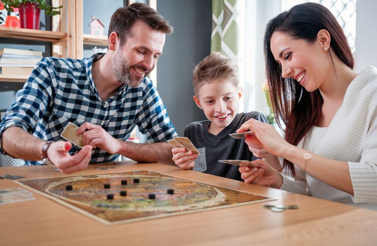 Weiße Familie (Vater, Mutter, Sohn) spielen zusammen ein Brettspiel am Esstisch