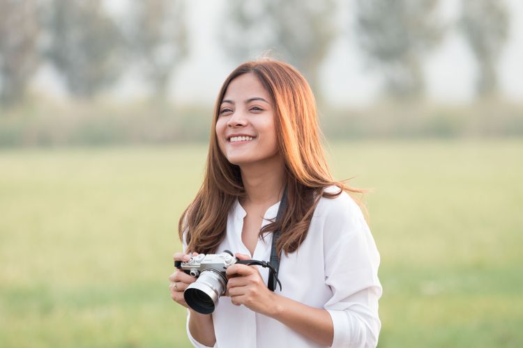 Junge lächelnde Fotografin outdoor mit einer Kompaktkamera mit Zoom-Objektiv.