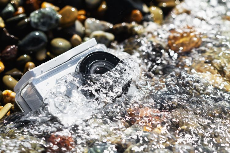 Weiße wasserdichte Kamera im Wasser am Kieselstrand.