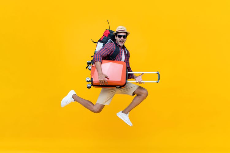 Urlauber springt mit Koffer im Arm in die Luft