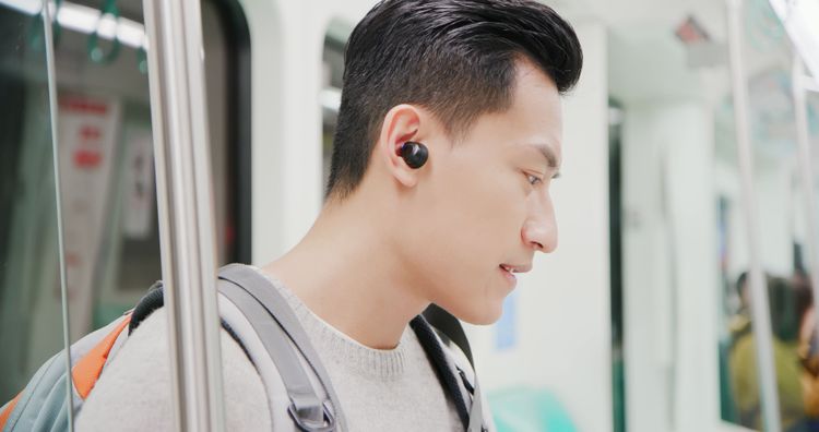 Junger asiatischer Mann mit Earbuds in der U-Bahn
