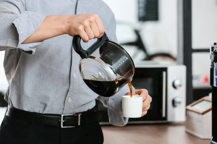 Person gießt aus Kaffeekanne in Kaffeetasse