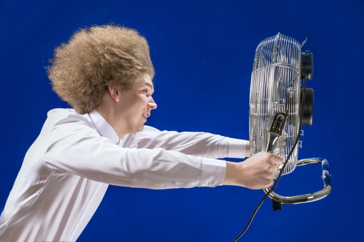 Mann setzt sich starkem Luftstrom eines Bodenventilators aus den er in Händen hält
