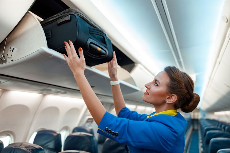 Stewardess verstaut Handgepäck in Kofferablage im Flugzeug