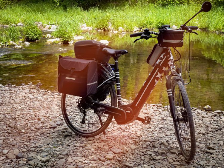Vollbeladenes E-Trekkingbike mit vielen Gepäcktaschen steht an einem Fluss