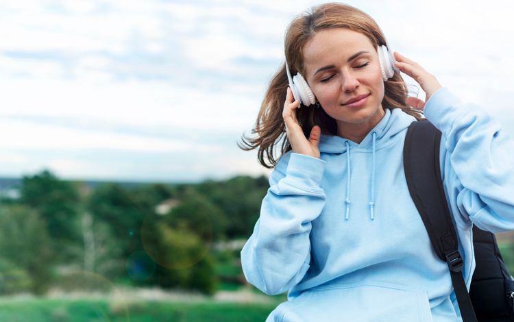 Junge Frau mit kabellosen Bluetooth-Kopfhörern in der Natur beim Musikhören mit geschlossenen Augen