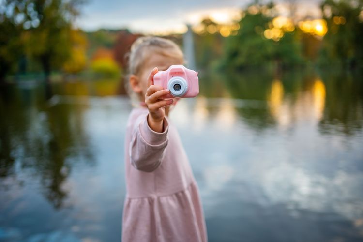 Kleines Mädchen mit einer pinken Kinderkamera vor einem Teich