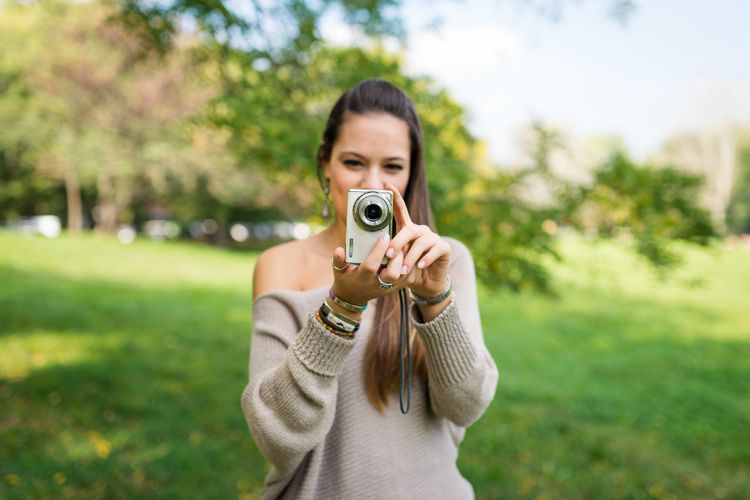 Portrait eine jungen Frau mit einer Kompaktkamera im Park