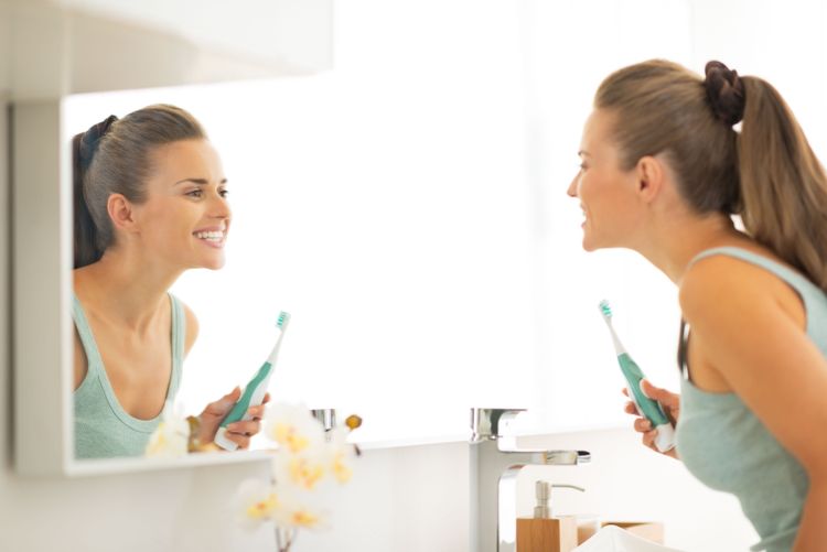 Junge Frau schaut sich nach dem Zähneputzen mit der Elektrozahnbürste in den Spiegel