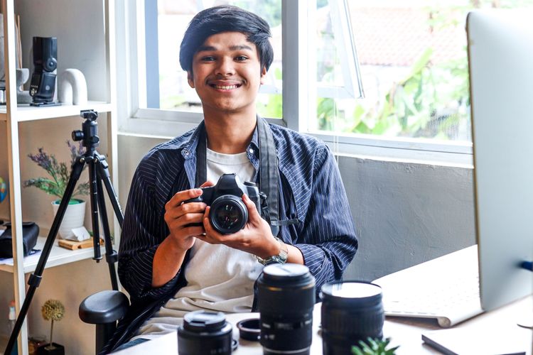 Junger asiatischer Fotograf mit Systemkamera und verschiedenen Objektiven