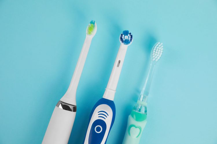 Schallzahnbürste, rotierende Zahnbürste und Kinder-Elektrozahnbürste nebeneinander auf blauem Hintergrund
