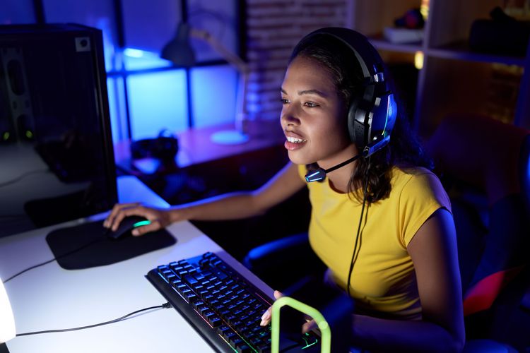 junge Frau mit großem Over-Ear Gaming-Headset vor dem Desktop-PC