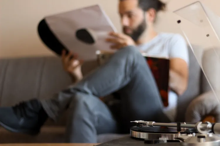 Bärtiger Mann betrachtet Vinyl-Cover auf Sofa