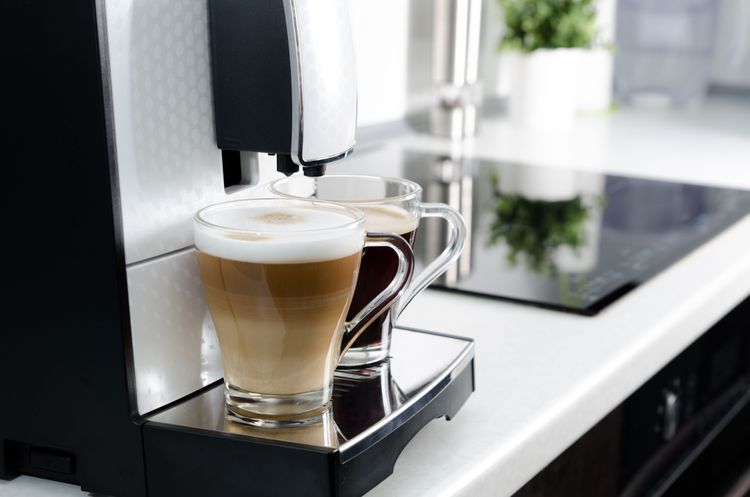 Zwei Gläser mit Cappuccino und Espresso unter dem Kaffeeauslauf eines Vollautomaten
