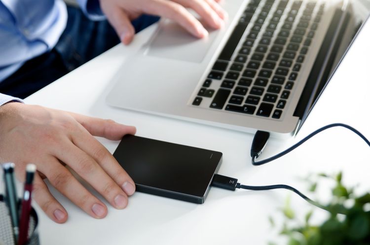 Männliche Hand an externer Festplatte, die an einen Laptop angeschlossen ist