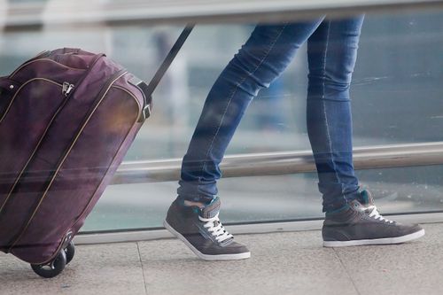 Person zieht Reisetasche mit Rollen hinter sich her