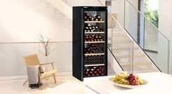 Gefüllter Weinkühlschrank in offenem Wohnraum neben einem Lehnstuhl.